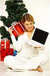 Young beautiful woman next to christmas tree, presents and laptop computer