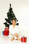 Young beautiful woman next to christmas tree and presents listen to music in headphones