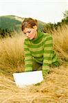 Young business woman working on laptop computer on golden meadow at mountains outdoors