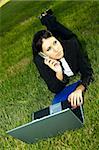 Business woman working on grass with laptop computer and talking cell phone