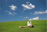 Beautiful young woman laying down on a green meadow with a flower