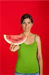 Beautiful young woman eating a slice of watermelon on a red background