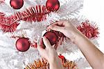 Female hands, hanging ornaments on a white Christmas tree.