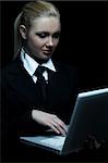 Beautiful business woman wearing black tie and jacket isolated on black background with laptop computer