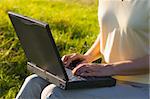 Woman typing on a laptop in a green meadow