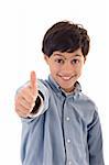 Cute kid smiling, wearing a blue shirt, showing a thumbs up against white background.