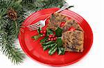 Delicious holiday fruitcake on a red plate garnished with holly.  White background with pine branches.