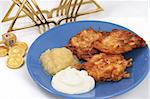 A Hanukah still life with potato latkes, dreidel, gelt (chocolate coins) and a menorah on a white background.