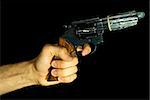 Male hand holding a revolver with a condom on it. Black background.