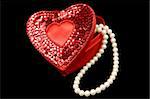 A red satin heart shaped box filled with pearls, isolated on a black background.