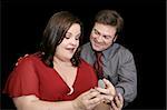 Beautiful plus sized model surprised by a marriage proposal.  Black background.