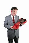 A handsome man in a suit holding an open heartshaped box of valentines chocolates.  Isolated on white.