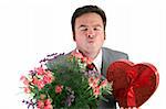 A man holding Valentines candy and flowers and puckering up for his thank you kiss.  Isolated on white.