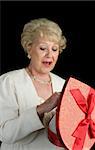 A beautiful senior woman choosing a chocolate from a box of Valentines candy.  Black background