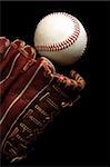 Close up of a baseball glove and a ball on a black background