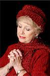 A beautiful senior lady in red with her hands folded in prayer.  Black background.