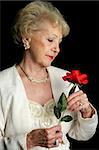 A beautiful senior lady holding a rose.  She is wearing a hearing aid.