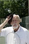 A hot and tired senior man wiping his brow after a tennis match.