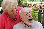 A senior couple joking around.  She is feeding him grapes.