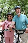 An attractive senior couple bicycling with helmets on.