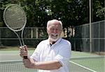 A handsome senior man on the tennis court getting ready for a game.