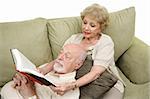 A senior man taking an afternoon nap while his wife reads to him.  White Background.