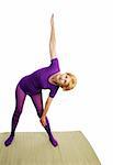 A fit seventy year old woman doing the triangle pose for yoga.  White background.