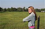 a beautiful girl on a ranch, leaning on a fence looking at a field, with a barn in the distance