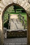 a rustic wooden bridge and small stone wall are framed by a limestone arch in this French park.