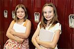 Two cute school girls leaning against their lockers.