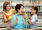 Two students giving apples to their favorite teacher.  She is very surprised and happy.