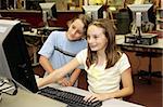 Two school children doing research together on the library computers.