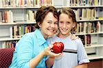 A cute school boy giving his teacher an apple.