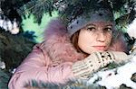 Beautiful girl in hat and mittens in snow-covered evergreens. Copy space on left top
