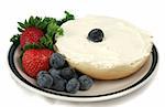 A bagel with cream cheese on a plate garnished with berries.