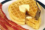 A closeup of waffles dripping with syrup and butter, with bacon strips on the side.