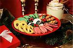 A plate of beautiful Christmas cookies and a mug of egg nog on the table beside pine branches and gifts.