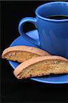 A closeup of biscotti and coffee against black background.