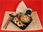 A delicious chinese dinner of hot & sour soup, fried fantail shrimp on a bamboo mat.  Complete meal with chopsticks & tea over red.