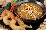Chinese hot & sour soup served with fried shrimp and crunchy noodles.  Closeup view.