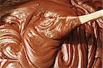 a closeup photo of a wooden spoon stirring a pot of melted chocolate fudge