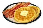 A plate of bacon strips and waffles dripping with syrup and butter.  Isolated.