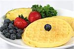 Closeup view of golden waffles served with berries and pineapple on the side.