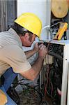 An air conditioning repairman using a voltage tester on a compressor unit.