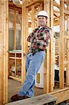 Full body view of a handsome construction worker leaning casually against a wood framed building.  Authentic construction worker on actual construction site.