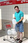 A man with a shopping cart full of water bottles in preparation for a hurricane.  Could also be used for recycling.