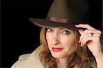 A beautiful woman in a smiling in a hat and trenchcoat over a black background.  Possible marital role playing.