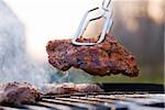 Delicious chuck steak on the grill in metal tongs. Shallow depth of field.