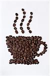 Coffee cup sign made of coffee seeds on the white table-cloth. Clipping path included.