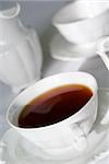 Cup of tea (focus only in the middle part of the cup edge) and porcelain milk jug and another cup behind on the white tablecloth. Shallow depth of field.